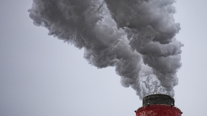 Ansicht eines Schornsteins vor grauem Himmel, aus dem große Rauchschwaden austreten