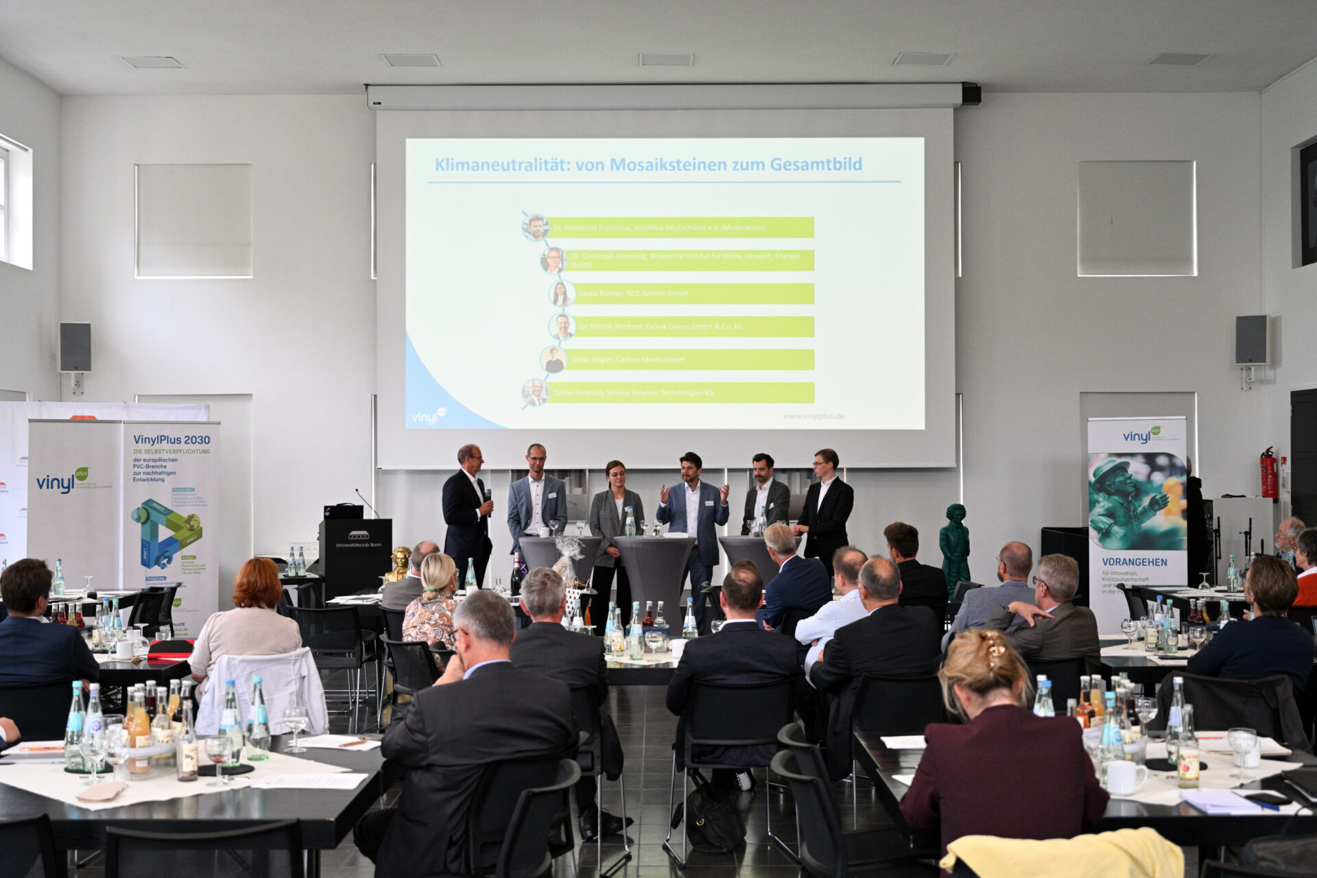 Mehrere Fachleute diskutieren beim Nachhaltigkeitsforum von Vinyl Plus Deutschland in Bonn auf einer Bühne vor Publikum über Klimaneutralität in der PVC-Branche.