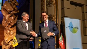 Die Politiker Jan Jambon und Hendrik Wüst reichen sich die Hand und halten ein Dokument, im Hintergrund das Logo von Circular Valley sowie die Flaggen von NRW und Flandern.