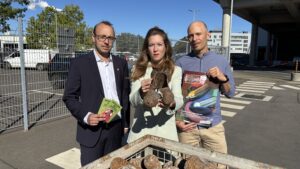 Drei Personen stehen vor einem Container mit entsorgten Lachgas-Kartuschen und halten Info-Materialien sowie eine Kampagnenbroschüre hoch. Aufgenommen vor dem Müllheizkraftwerk Ruhleben.