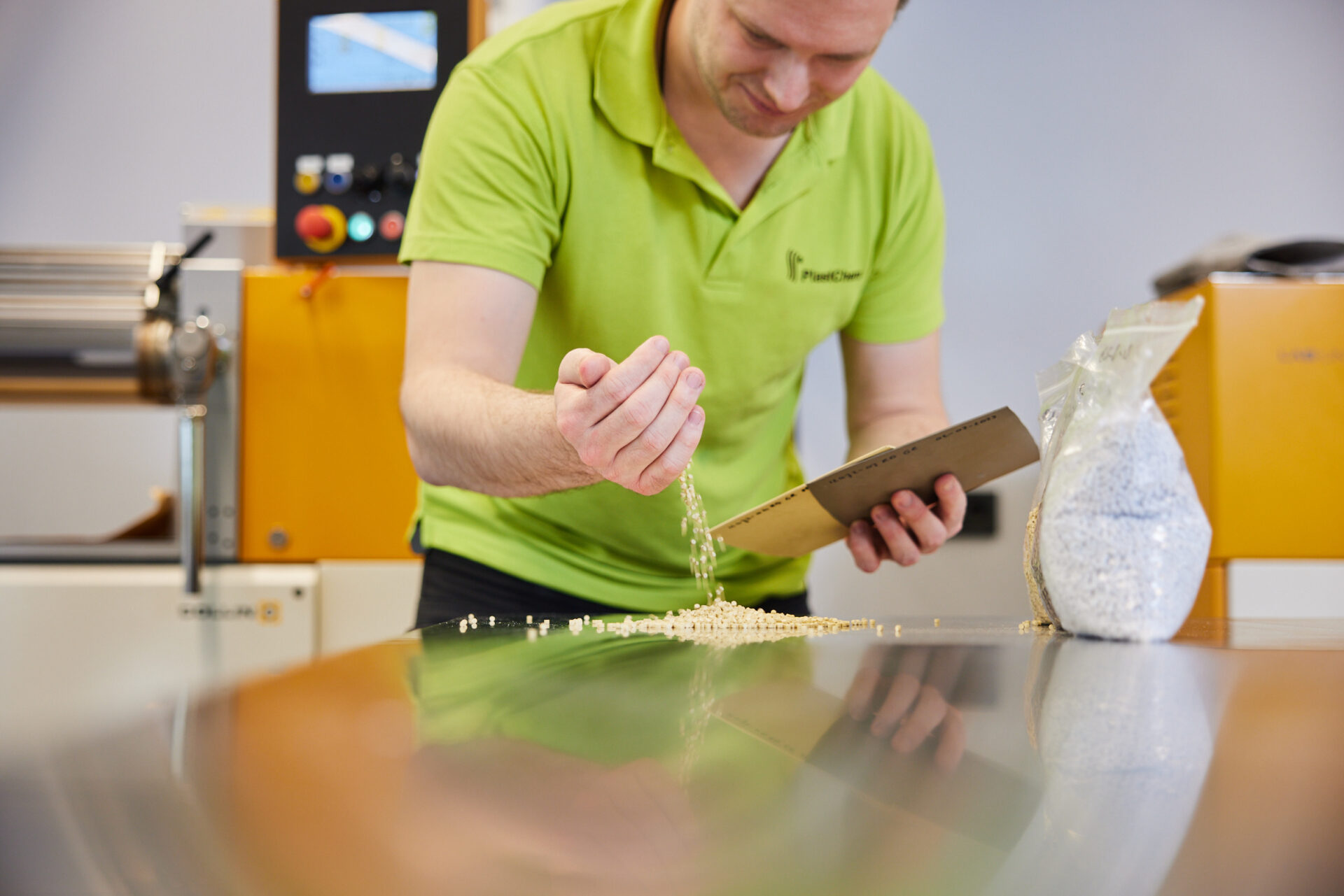 Ein Mann betrachtet Kunststoffgranulat, das er auf einen Tisch rieseln lässt