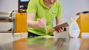 Ein Mann betrachtet Kunststoffgranulat, das er auf einen Tisch rieseln lässt