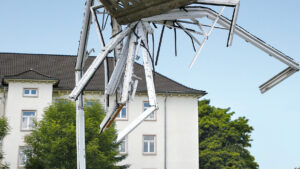 Ein Bagger mit Greifarm hebt alte PVC-Fensterrahmen auf einen Haufen vor einem Gebäude, um sie für das Recycling zu verladen.