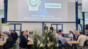 Dr. Frank Albers und Christina Guth stehen auf einer Bühne im Krone-Trailer-Forum und sprechen zur Eröffnung des zweiten Azur-Runderneuerungsgipfels 2025 vor den Teilnehmenden.