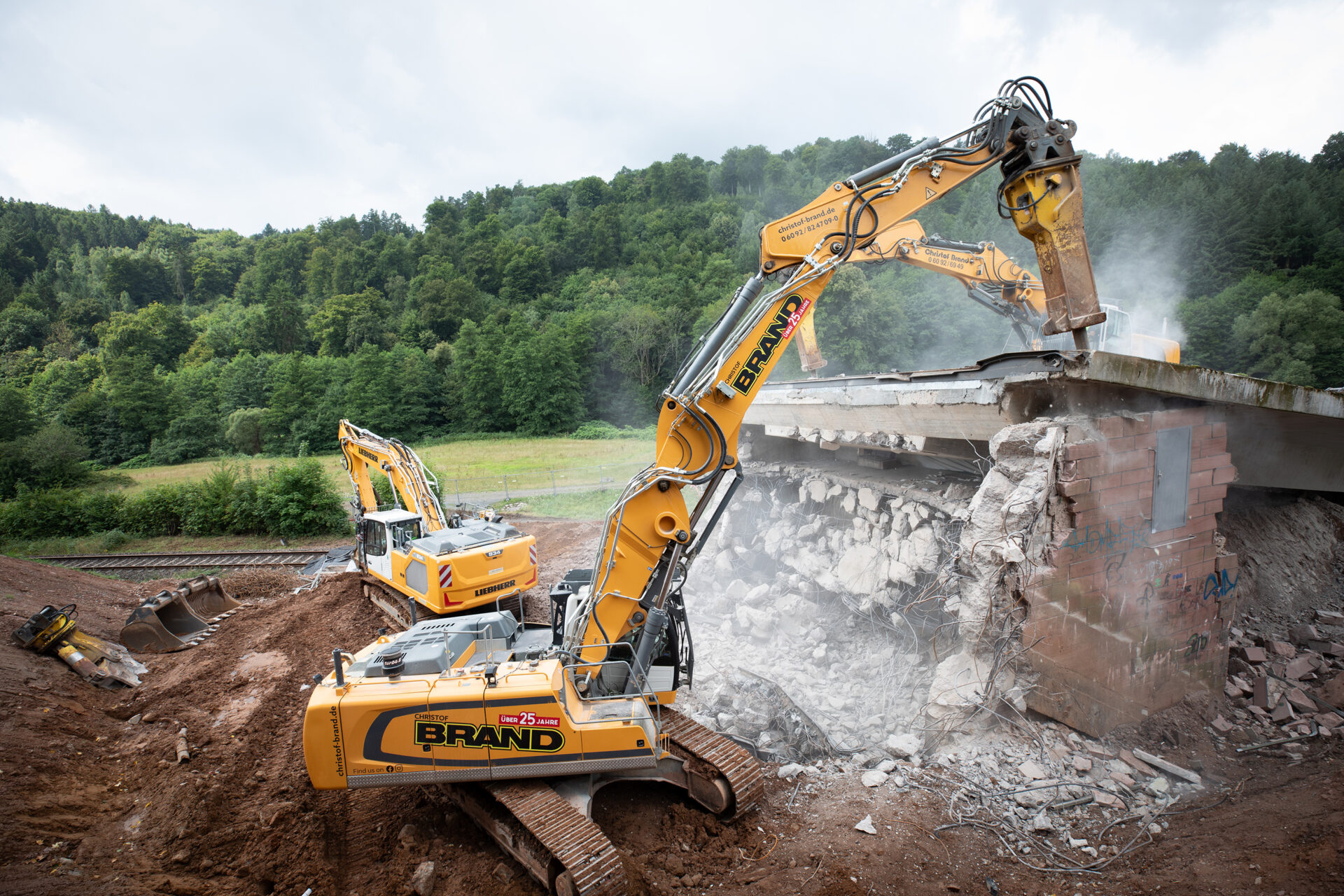 Zwei gelbe Liebherr-Bagger beim kontrollierten Abbruch der Zeller Brücke im Odenwald, die mit Hydraulikhämmern die Brückenteile zerkleinern.