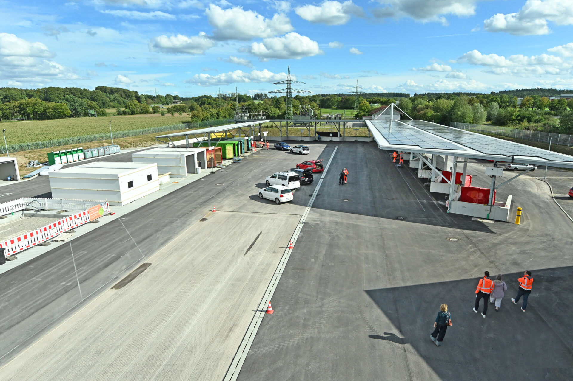 Luftaufnahme des neuen Wertstoffzentrums in Gilching mit Zufahrtsbereich, Containern, Photovoltaik-Dach und Besuchern auf dem Gelände.