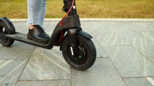 Nahaufnahme eines E-Scooters mit sichtbarem Vorderrad, gefahren von einer Person in schwarzen Schuhen